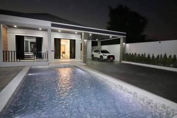 Modern house exterior at night with illuminated swimming pool and parked car
