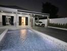 Modern house exterior at night with illuminated swimming pool and parked car