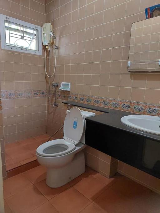 Compact bathroom with wall-mounted water heater, ventilation window, toilet, and vanity countertop