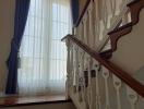Elegant staircase with wooden handrails and large window with curtains