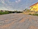 Empty residential land plot with gravel surface near buildings under a cloudy sky