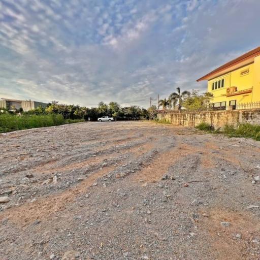 Empty residential land plot with gravel surface near buildings under a cloudy sky