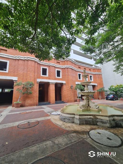 Exterior view of a brick building with a decorative fountain and greenery