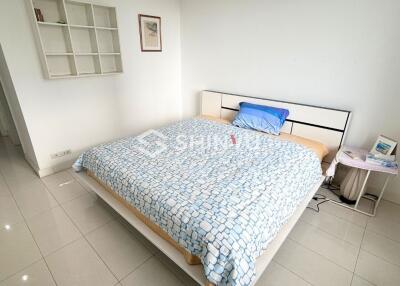 Bedroom with a white tiled floor, a bed with a patterned blue and white bedspread, and a wall-mounted shelf