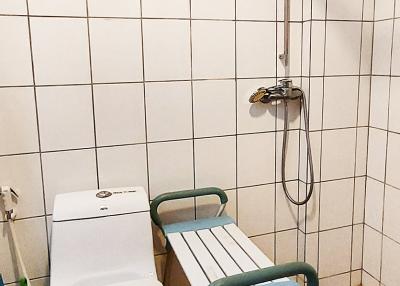 Compact bathroom with white tiling, wall-mounted water heater, and accessibility aids