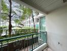 Spacious balcony with a view of green outdoor area and neighboring buildings