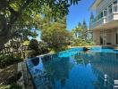 Luxurious outdoor pool with crystal clear water bordered by lush greenery and a view of a modern house