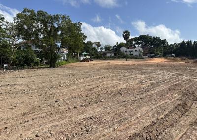 Large empty land plot ready for construction with nearby trees and residential structures in the background