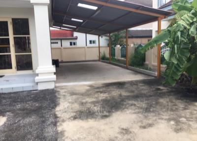 Spacious driveway in front of a residential building with carport and tropical foliage