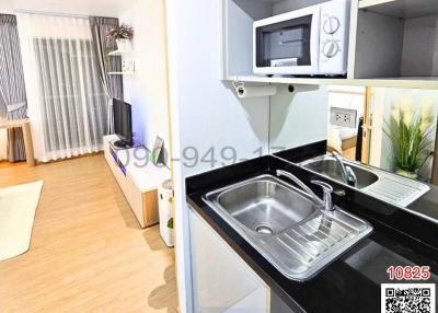 Modern open-plan living room with attached kitchenette featuring stainless steel sink and built-in microwave