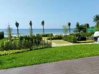 Spacious beachfront garden with lush grass, wooden deck, and ocean view