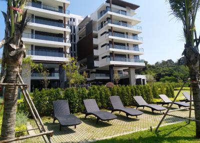 Modern multistory building exterior with landscaped garden and lounging chairs