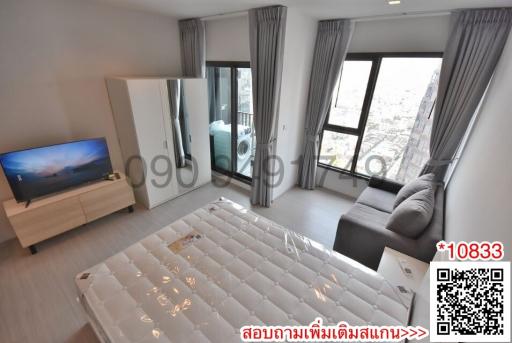 Modern bedroom with city view through large windows, including a bed, TV, and seating area