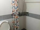 Compact bathroom with white toilet, wall-mounted shower, and patterned shower curtain