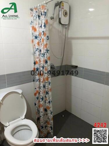 Compact bathroom with white toilet, wall-mounted shower, and patterned shower curtain