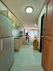 Long narrow kitchen with white appliances leading to a bright living area