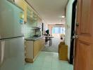 Long narrow kitchen with white appliances leading to a bright living area