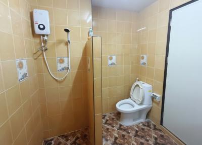 Compact bathroom with tiled walls and floor, featuring a toilet, shower, and water heater