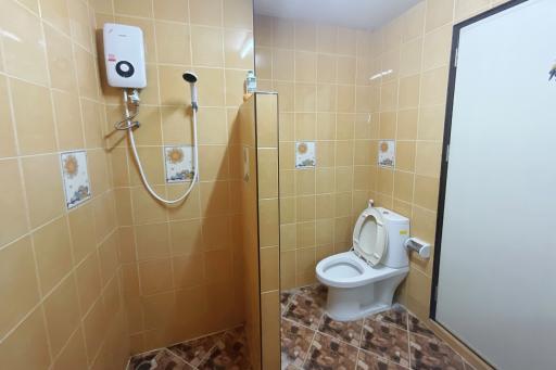 Compact bathroom with tiled walls and floor, featuring a toilet, shower, and water heater