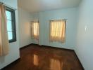 Spacious and bright empty bedroom with hardwood floors and large windows with curtains