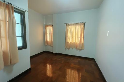 Spacious and bright empty bedroom with hardwood floors and large windows with curtains