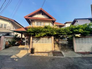 Two-story residential house with a gated entrance and green foliage