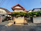 Two-story residential house with a gated entrance and green foliage