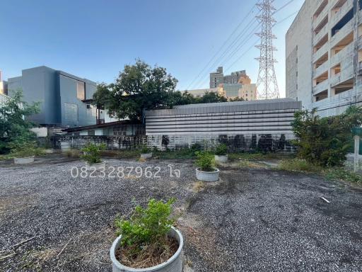 Exterior view of a vacant lot with buildings and power lines in the background