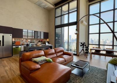 Spacious living room with high ceilings, large windows, and modern kitchen in the background