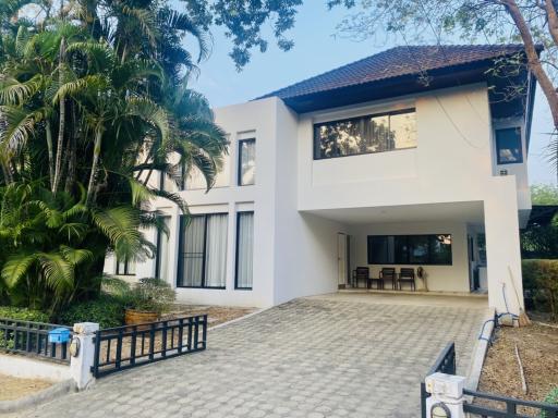 Modern two-story house with large windows and a tiled driveway surrounded by lush greenery