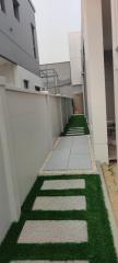 Side pathway between buildings with artificial grass lining and stepping stones