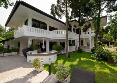 Spacious white two-story house with balconies, surrounded by lush greenery