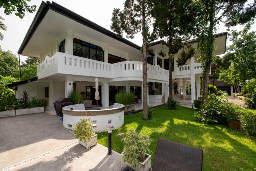 Spacious white two-story house with balconies, surrounded by lush greenery