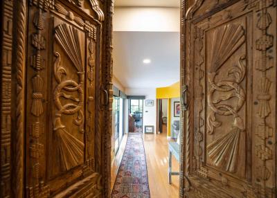 View through ornate wooden doors into a well-lit hallway of a house