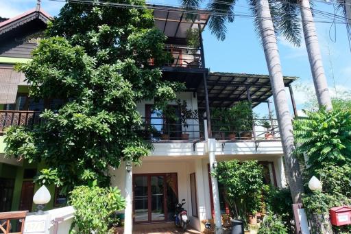 Tropical style multi-story house surrounded by lush greenery with a scooter parked in front