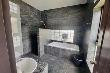 Modern bathroom with dark tiles, bathtub and glass block window