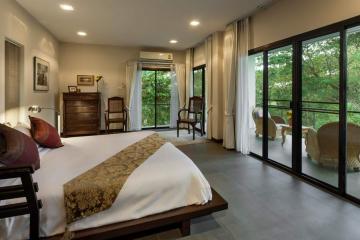 Spacious bedroom with a king-sized bed, large windows, and balcony access overlooking greenery