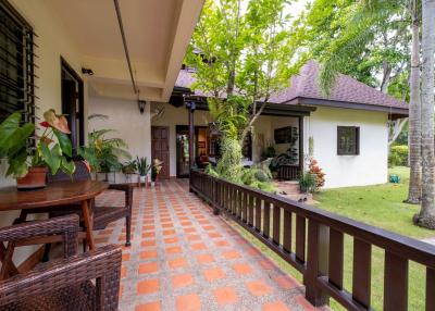 Spacious tiled patio with wooden railings leading to a house entrance surrounded by lush greenery