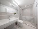 Modern white bathroom interior with glass shower enclosure, bathtub, and bright lighting