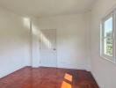 Bright empty bedroom with hardwood floors and a large window