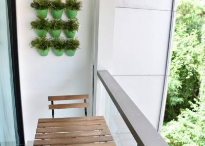 Compact balcony with a wooden table and chairs set, a wall-mounted plant decoration, and overlooking greenery