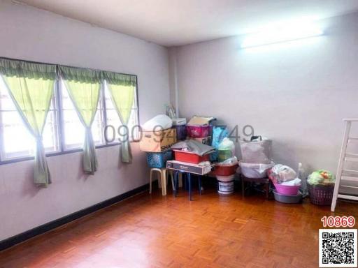 Cluttered bedroom with wooden flooring and curtained windows