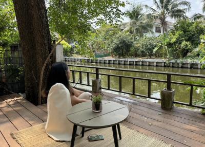 Person relaxing on riverside patio with greenery