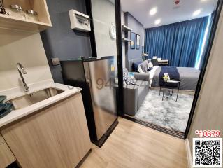 Modern kitchen with stainless steel appliances adjacent to cozy living space with blue curtains and plush rug