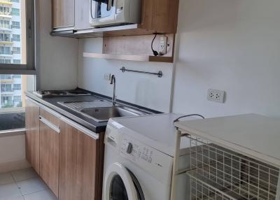 Compact kitchen with modern appliances including microwave, stove, and washing machine