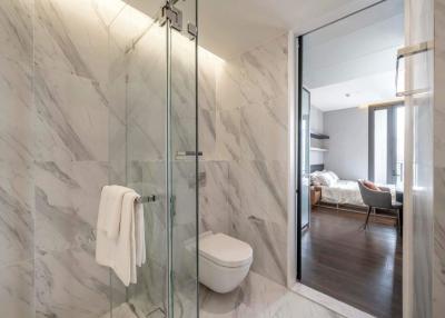 Modern bathroom with marble tiles and glass shower cabin leading to a bedroom