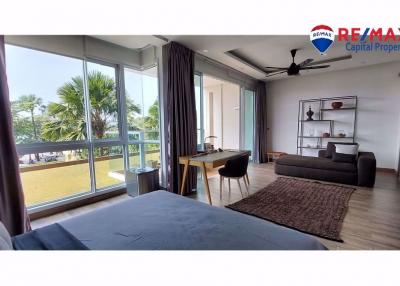 Spacious bedroom with large windows and a view, featuring a bed, a work desk, and a comfortable sitting area