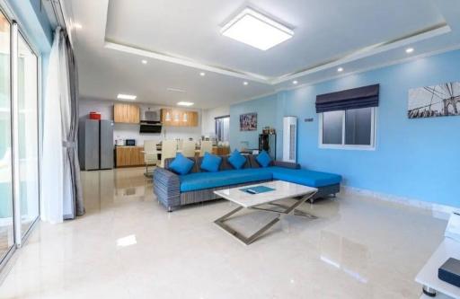 Spacious living room with modern open kitchen, bright blue accents and glossy floor tiles