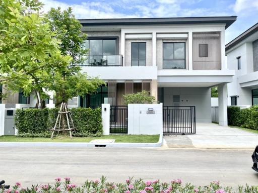 Modern two-story house with a gray facade and balcony, front yard with greenery and a gated entry