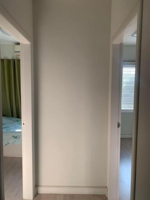 View of a clean, narrow hallway leading to a bedroom with a glimpse of green curtains and blinds